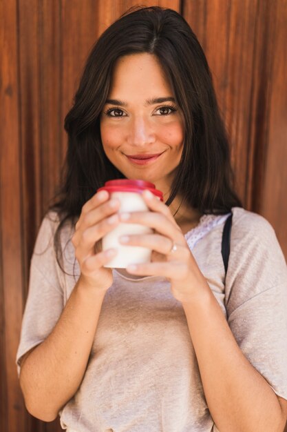 Il ritratto sorridente di una tenuta della ragazza porta via la tazza di caffè