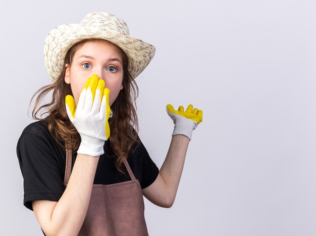 Il sacro giovane giardiniere che indossa un cappello da giardinaggio con guanti punta dietro il viso coperto con la mano