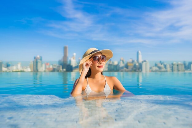 Il sorriso della bella giovane donna asiatica del ritratto si rilassa il tempo libero intorno alla piscina all'aperto con la vista della città