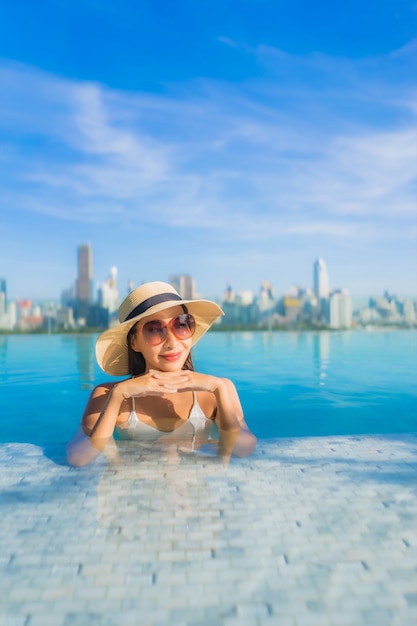 Il sorriso della bella giovane donna asiatica del ritratto si rilassa il tempo libero intorno alla piscina all'aperto con la vista della città