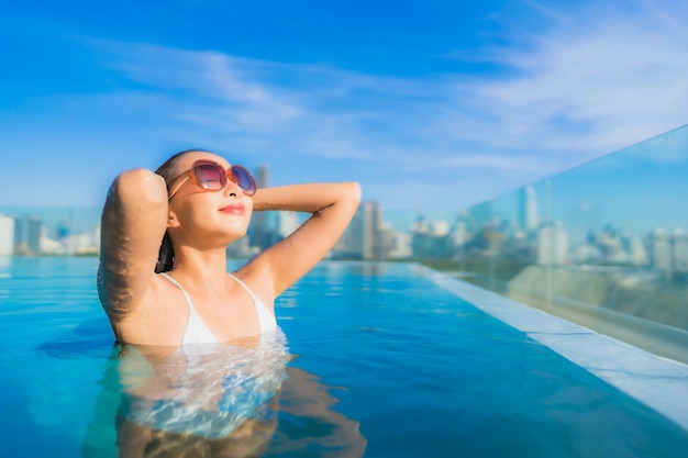 Il sorriso della bella giovane donna asiatica del ritratto si rilassa il tempo libero intorno alla piscina all'aperto con la vista della città