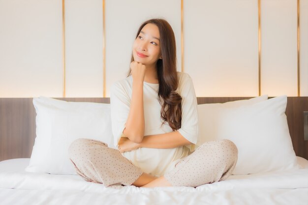 Il sorriso della bella giovane donna asiatica del ritratto si rilassa il tempo libero sul letto nell'interno della camera da letto