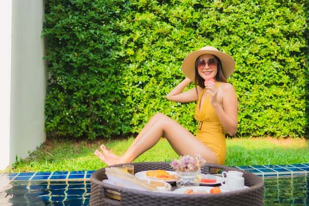 Il sorriso felice della bella giovane donna asiatica del ritratto si rilassa con la prima colazione che galleggia intorno alla piscina