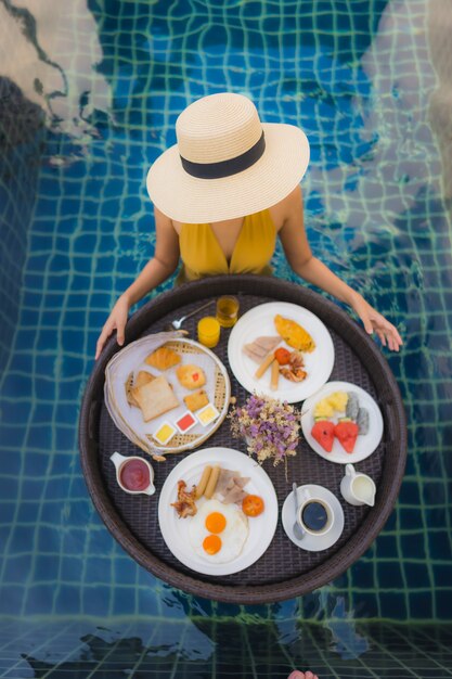 Il sorriso felice della bella giovane donna asiatica del ritratto si rilassa con la prima colazione che galleggia intorno alla piscina