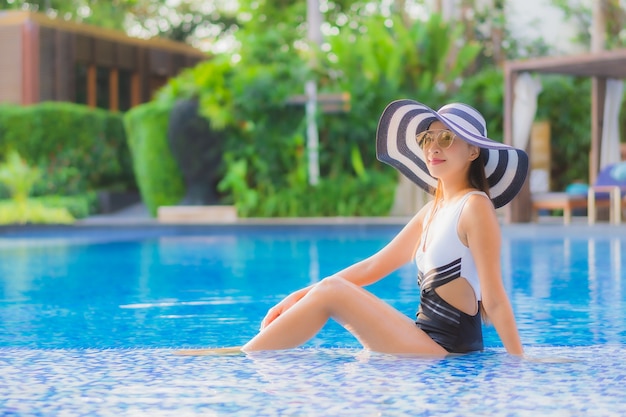 Il sorriso felice della giovane donna asiatica del bello ritratto si rilassa intorno alla piscina nell'hotel di località di soggiorno