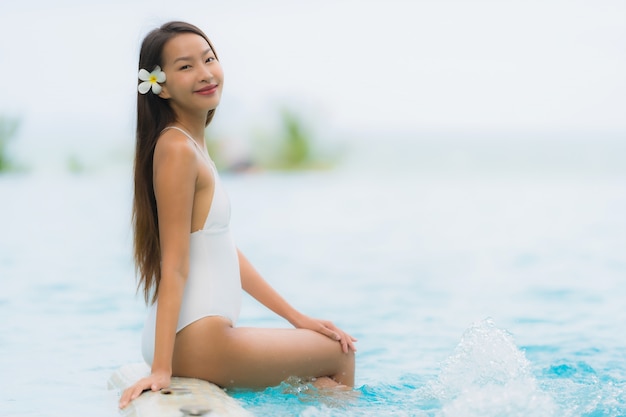 Il sorriso felice della giovane donna asiatica del ritratto si rilassa intorno alla piscina nella località di soggiorno dell'hotel