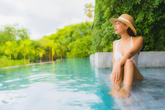 Il sorriso felice delle belle giovani donne asiatiche del ritratto si rilassa intorno alla piscina all'aperto in hotel