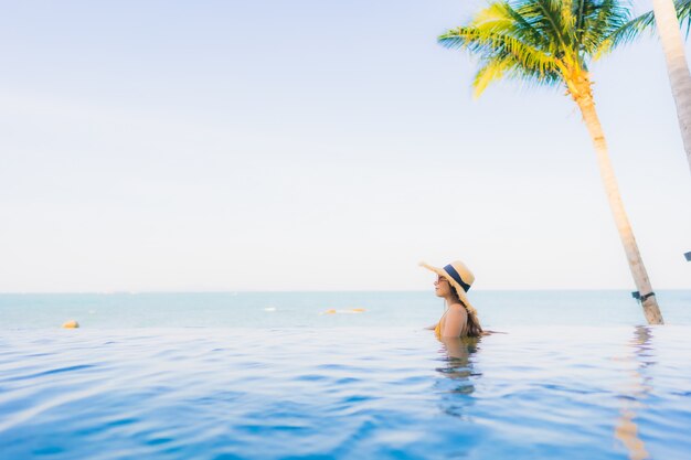 Il sorriso felice delle belle giovani donne asiatiche del ritratto si rilassa intorno alla piscina all'aperto