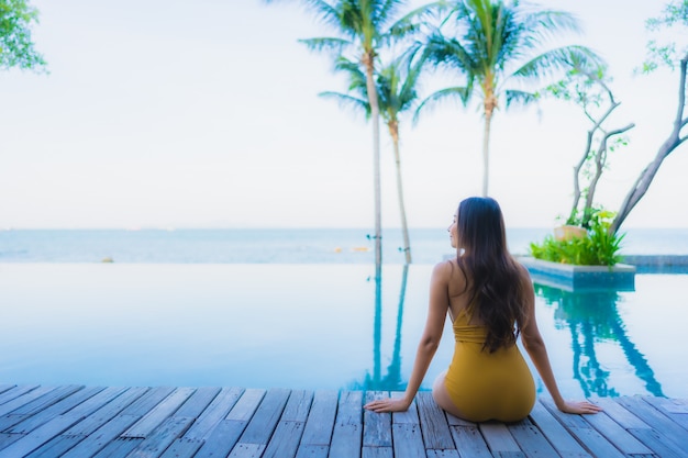 Il sorriso felice delle belle giovani donne asiatiche del ritratto si rilassa intorno alla piscina all'aperto