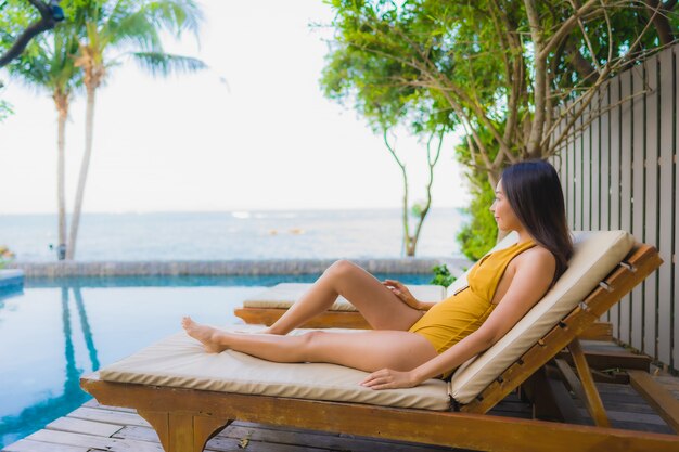 Il sorriso felice delle belle giovani donne asiatiche del ritratto si rilassa intorno alla piscina all'aperto