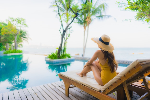 Il sorriso felice delle belle giovani donne asiatiche del ritratto si rilassa intorno alla piscina all'aperto