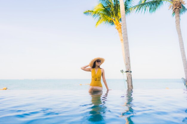 Il sorriso felice delle belle giovani donne asiatiche del ritratto si rilassa intorno alla piscina all'aperto