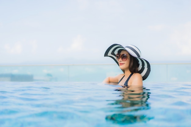 Il sorriso felice delle belle giovani donne asiatiche del ritratto si rilassa la piscina all'aperto nella località di soggiorno