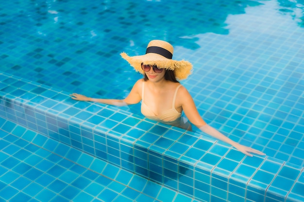 Il sorriso felice delle belle giovani donne asiatiche del ritratto si rilassa la piscina all'aperto nella località di soggiorno