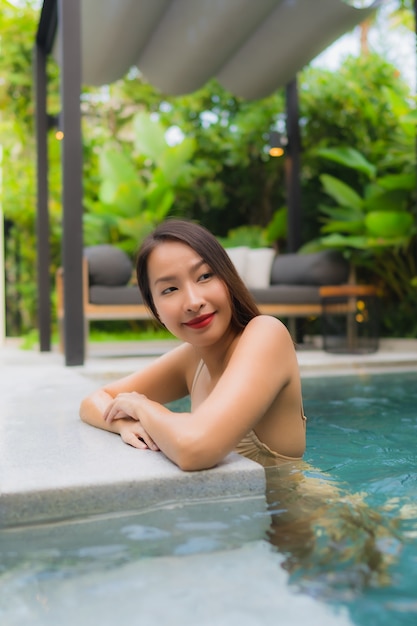 Il sorriso felice delle belle giovani donne asiatiche del ritratto si rilassa la piscina all'aperto nella località di soggiorno