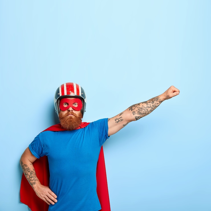 Foto gratuito il supereroe serio e fiducioso finge di volare, indossa mantello rosso, maschera, casco protettivo