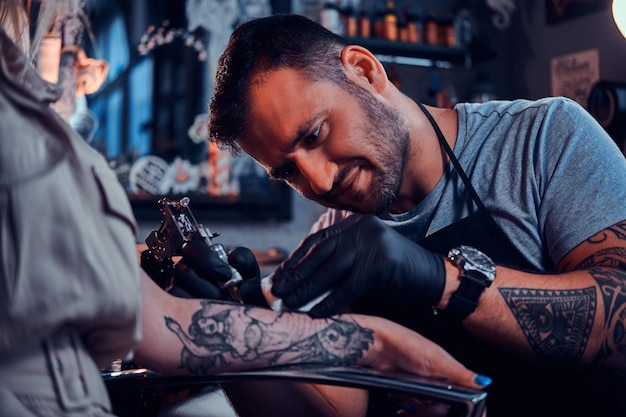 Il tatuatore diligente e concentrato sta creando un nuovo tatuaggio sulla mano di una giovane donna allo studio di tatuaggi.