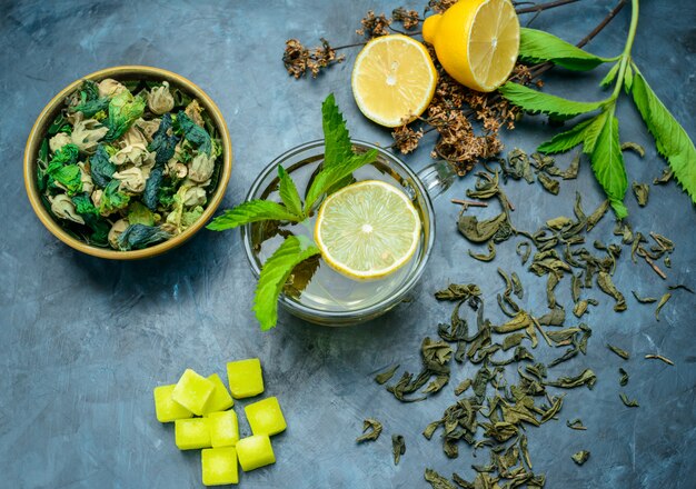 Il tè in una tazza con limone, menta, erbe essiccate, zollette di zucchero distese su una superficie blu