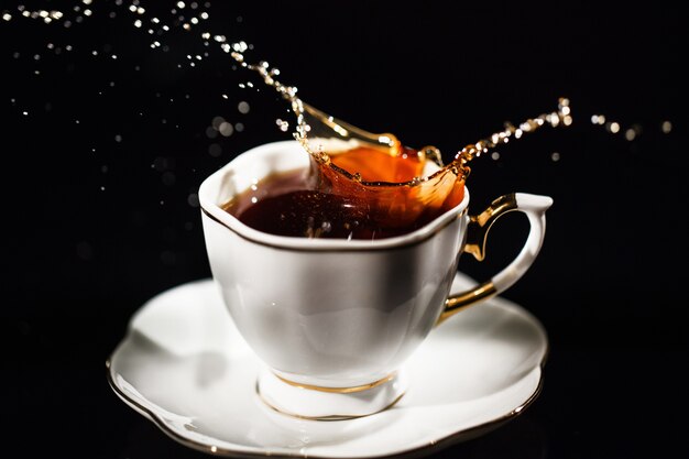 Il tè spruzza in tazza bianca su priorità bassa nera