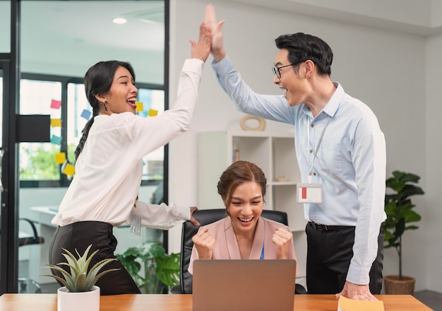 Il team di business asiatico sorride e alza le mani in alto festeggiando sentirsi felici e completare il lavoro di squadra