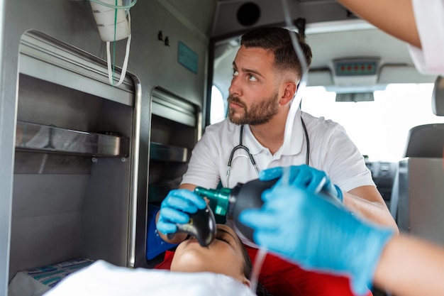 Il team di paramedici EMS fornisce assistenza medica al paziente ferito sulla strada per l'assistenza sanitaria Assistente per le emergenze ospedaliere utilizzando una maschera di ventilazione non invasiva in un'ambulanza Primo piano