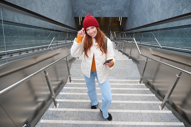 Il turista della ragazza dai capelli rossi ritratto sale le scale con lo smartphone segue il percorso sulle prese dell'app del telefono cellulare