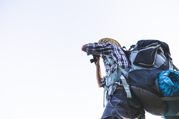 Il turista sta guardando attraverso il binocolo sul soleggiato cielo nuvoloso dalla cima della montagna.