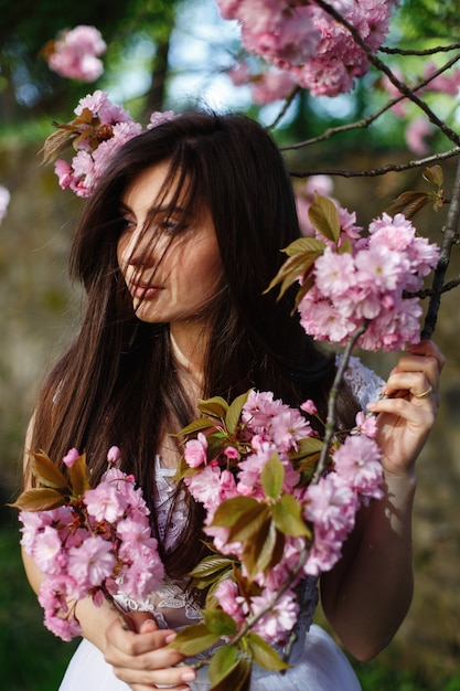 Il vento soffia i capelli della donna bruna mentre posa davanti a un albero in fiore di sakura