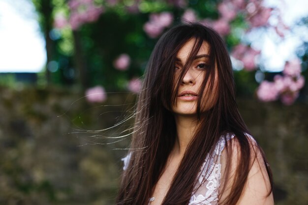 Il vento soffia i capelli della donna bruna mentre posa davanti a un albero in fiore di sakura