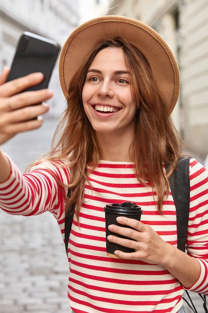 Il viaggiatore abbastanza contento fa clic sulla foto del selfie, crea nuove foto, utilizza il cellulare e l'applicazione