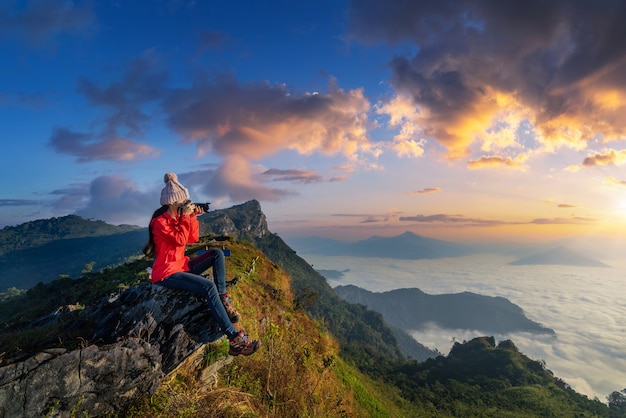 Il viaggiatore che si siede sulla roccia e che tiene la macchina fotografica prende la foto alle montagne di Doi pha mon a Chiang rai, Tailandia