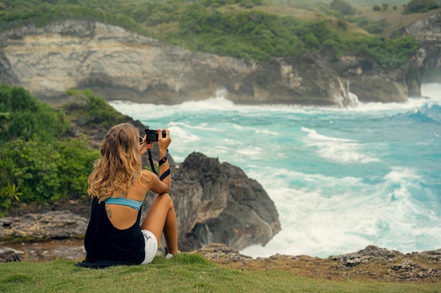 Il viaggiatore del fotografo della giovane donna con una macchina fotografica sul bordo di una scogliera prende le immagini della natura