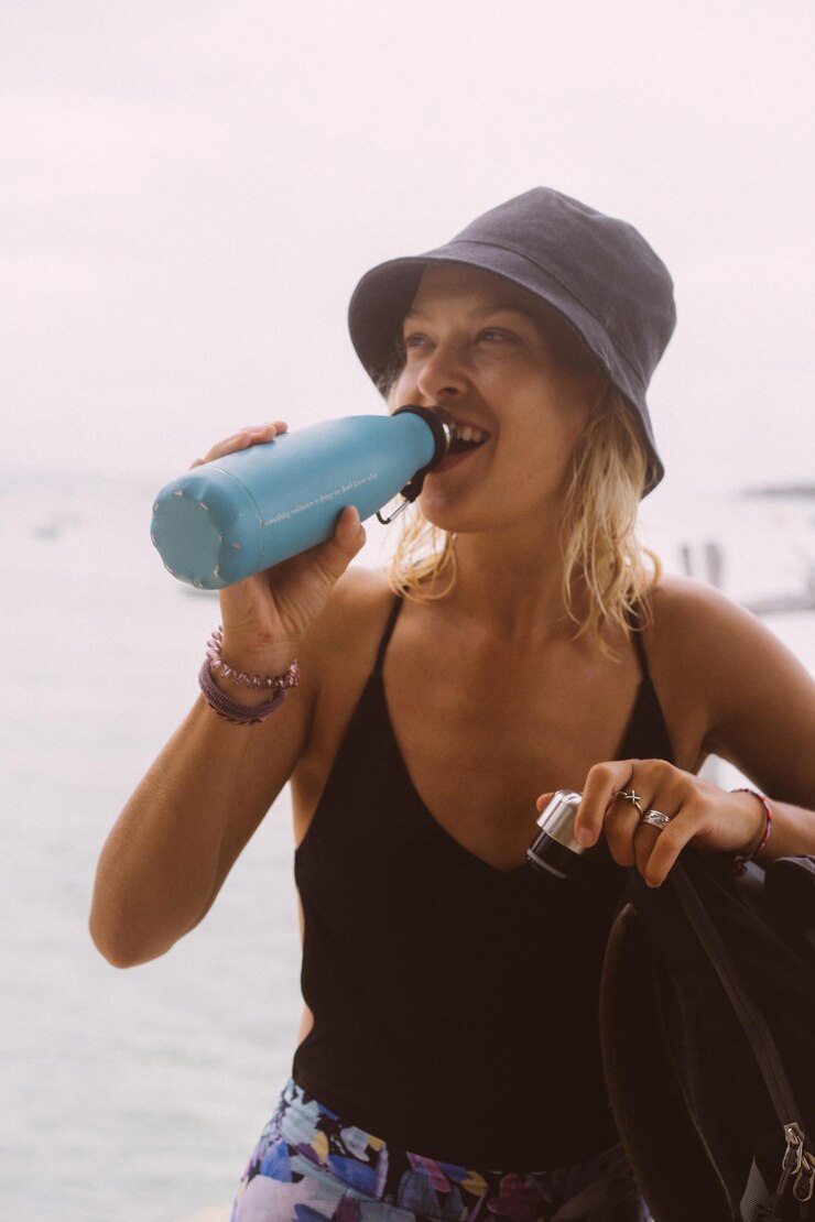 Il viaggiatore della giovane donna beve l'acqua da una bottiglia colorata.