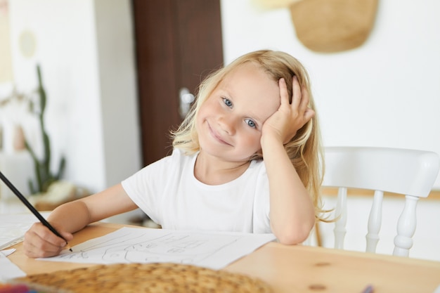 Immaginazione, arte, apprendimento, tempo libero e concetto di sviluppo dei bambini. Bel ragazzo biondo caucasico con sorriso carino e occhi azzurri, tenendo la matita, godendo di disegno e colorazione