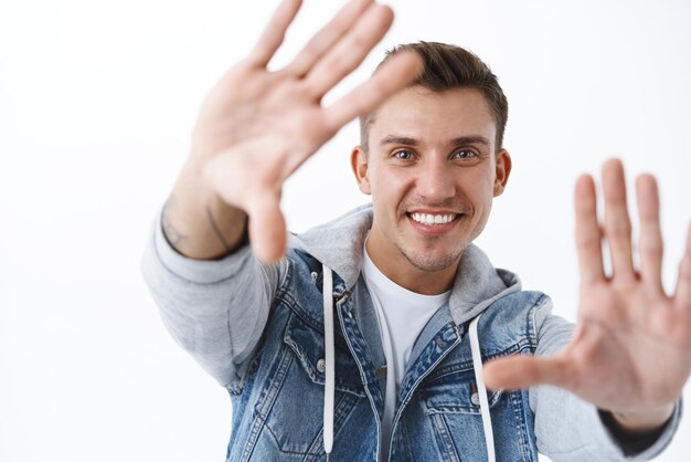 Immaginazione creatività e concetto di persone Ritratto del primo piano dell'uomo sorridente biondo bello sognante che immagina qualcosa che cattura il momento guarda attraverso le mani con il fondo bianco della faccia felice