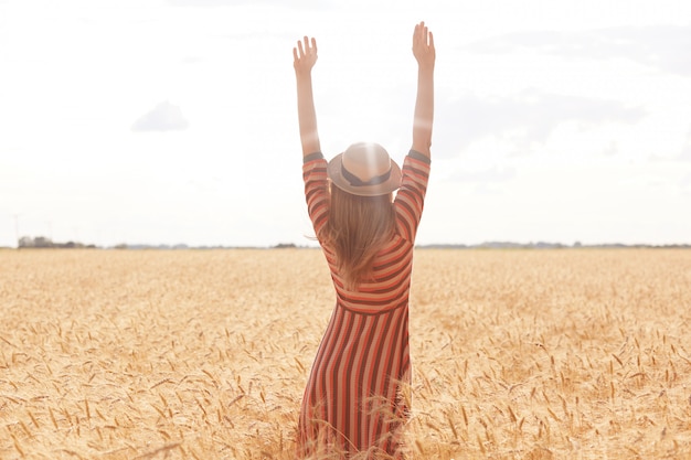 Immagine all'aperto della giovane donna alta positiva che tira le sue braccia su al sole