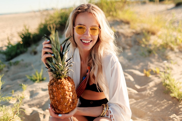 Foto gratuito immagine all'aperto di stile di vita di ridere bella donna con ananas succoso rilassante sulla spiaggia assolata. vestito estivo alla moda
