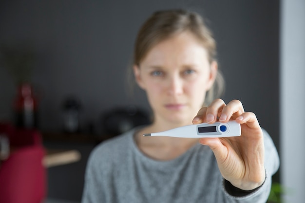 Immagine concentrata del termometro tenuta dalla giovane donna malata