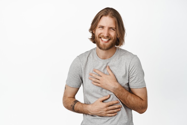 Immagine del bel ragazzo biondo caucasico, uomo barbuto che ride e sorride spensierato, faccia felice del giovane modello maschile in maglietta grigia, sfondo bianco.