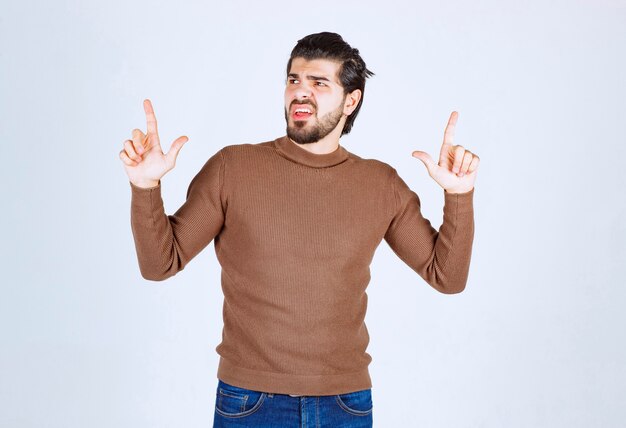 Immagine del giovane modello maschile in maglione marrone in piedi sul muro bianco.