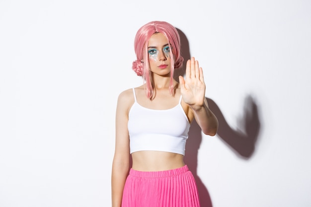 Immagine del modello femminile serio in parrucca rosa e costume di Halloween che mostra il segnale di stop