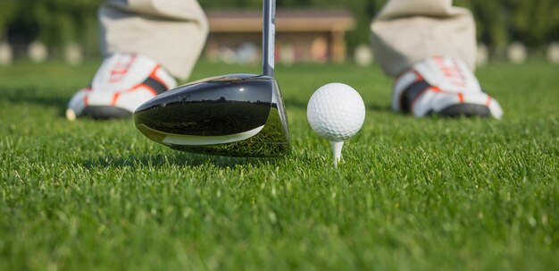 Immagine del primo piano della pallina da golf dietro il conducente al campo pratica in abbondanza di copyspace e profondità di campo molto ridotta