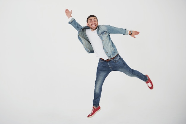Immagine del salto casuale vestita allegra del giovane sopra il bianco