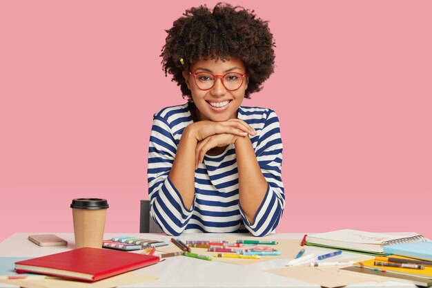 Immagine dell'adolescente felice con un sorriso a trentadue denti, tiene le mani sotto il mento, si rallegra dei commenti positivi sul suo lavoro