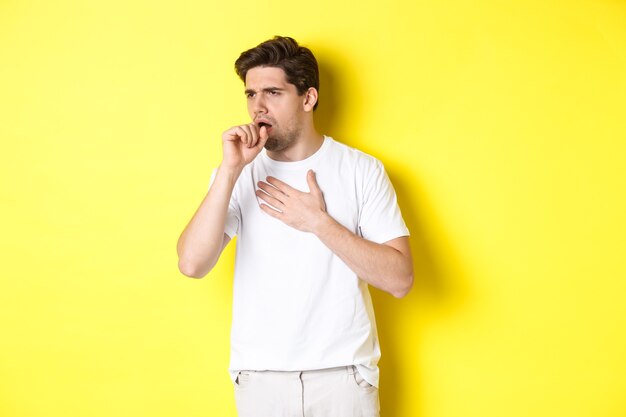 Immagine dell'uomo con covid-19 o sintomi influenzali, tosse e nausea, in piedi su sfondo giallo. Copia spazio