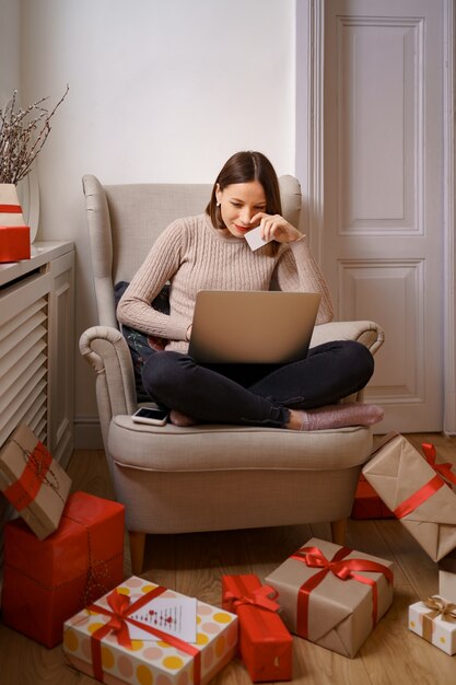 Immagine della carta di credito piacevole della tenuta della donna piacevole con lo spazio della copia facendo uso del laptop