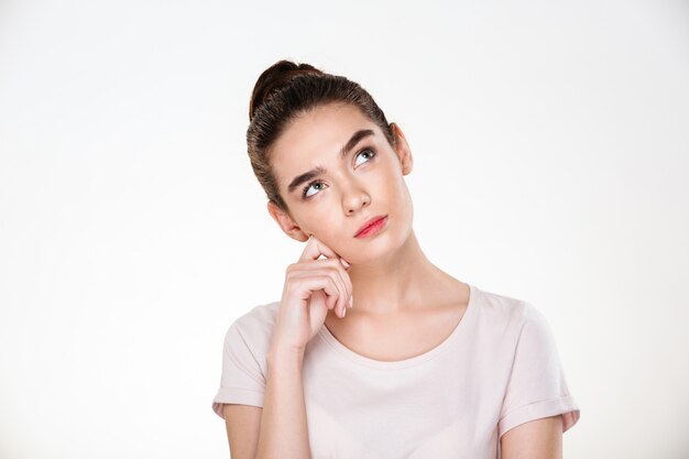 Immagine della donna seria con capelli castani in panino con il pensiero ascendente del fronte o il sogno della posa