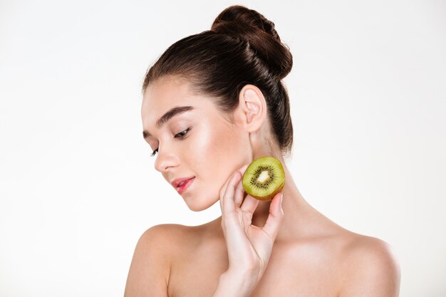 Immagine della donna tenera che ha pelle pulita che posa con gli occhi chiusi che giudicano disponibile il kiwi succoso maturo