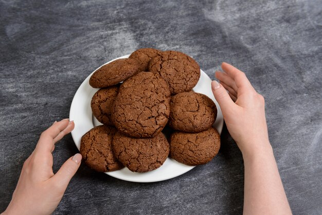Immagine delle mani che tengono i biscotti del cioccolato sopra superficie di legno