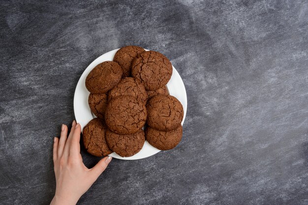 Immagine delle mani che tengono i biscotti del cioccolato sopra superficie di legno